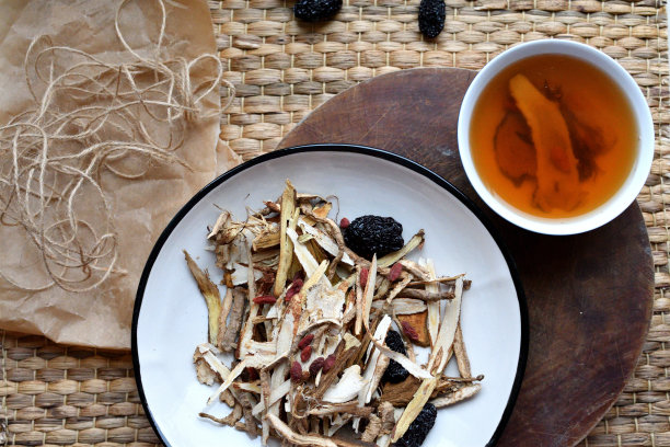 中药。用红枣、枸杞、人参等草药茶放在白色的盘子里，在中性的背景上。侧视图和俯视图。图片下载