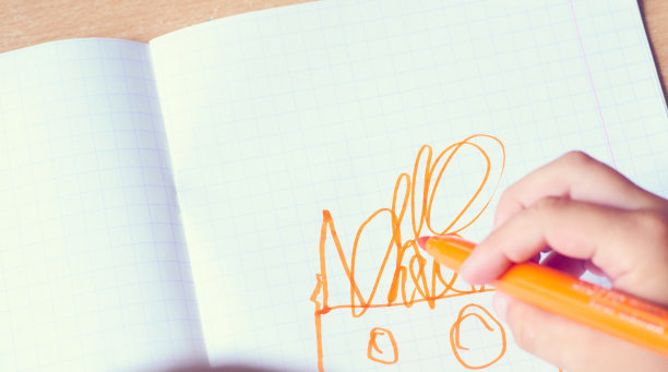 孩子的手用橙色毡尖笔在笔记本上画画。孩子们的创造力。图片下载