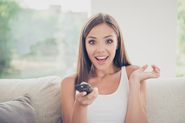 人们在闲暇时间表达自己的情感，表达幸福的观念。近距离的照片肖像pretty可爱的美丽与牙齿微笑愉快的女士拿着遥控器的手图片下载