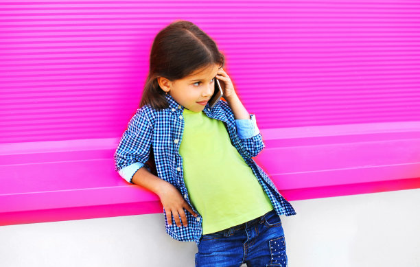 一个小女孩在城市街道上用智能手机打电话，背景是彩色的粉红色墙壁图片下载