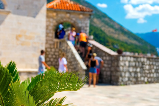 的背景图片。背景是模糊的游客景观，一座古老的建筑，群山和蓝天。在前景部分的混凝土墙和绿色植物，黑山图片下载