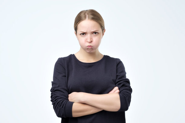 肖像美丽的女孩皱眉她的脸在不高兴，穿着黑色毛衣，保持双臂交叉。图片下载
