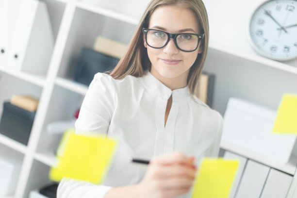 一个年轻的女孩站在办公室旁边，贴着贴纸。女孩手里拿着一杯咖啡。图片下载
