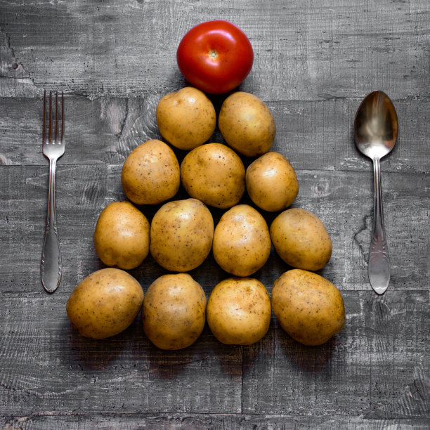 把一些土豆和一个西红柿放在一张旧木桌或木头表面上，摆成圣诞树的形状。布局俯视图图片下载