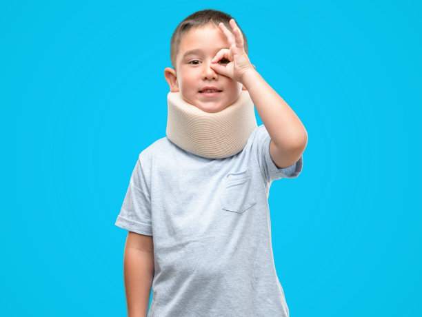 黑头发受伤的小孩戴着颈圈，面带笑脸，做着ok手势，手放在手上，眼睛透过手指看图片下载