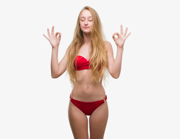 金发少女穿着红色比基尼放松和微笑闭着眼睛做冥想手势与手指。瑜伽的概念。图片下载