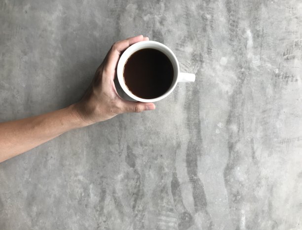 在咖啡店的水泥板桌子上，一个女人拿着一杯美式咖啡图片下载