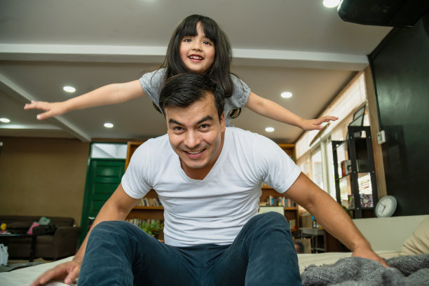 周末温馨时刻：爸爸和可爱的女儿在床上玩飞机图片下载