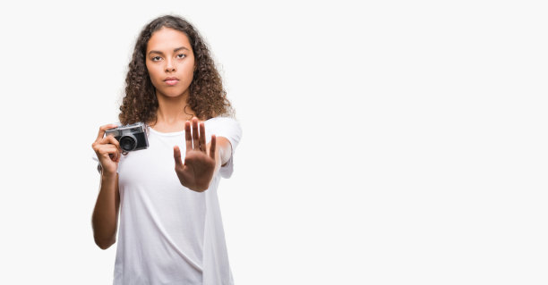 年轻的西班牙女性用老式相机拍照，张开手做着严肃和自信的表情，防御手势图片下载