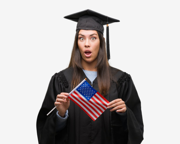 年轻的西班牙裔妇女穿着毕业制服举着美国国旗吓了一跳，脸上带着惊讶，害怕和兴奋的恐惧表情图片下载