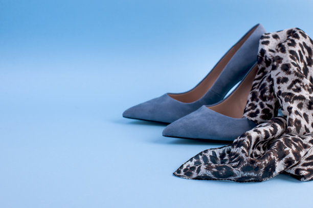 蓝色麂皮细高跟鞋和一条围巾。在蓝色背景上。女性的优雅的鞋子。文本的空闲空间。强光照在照片上。图片下载