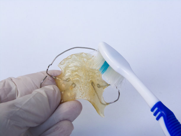 牙科医生用牙刷清洁可移动的牙齿矫正器。白色背景。图片下载