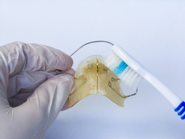 牙科医生用牙刷清洁可移动的牙齿矫正器。白色背景。图片下载