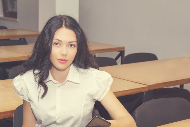 可爱的女孩坐在课桌上使用智能手机。教育理念的照片图片下载