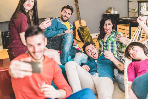 快乐的朋友用智能手机自拍，在家庭聚会上听音乐——年轻人喝酒，享受新千禧一代的潮流——关注中心女人的脸图片下载