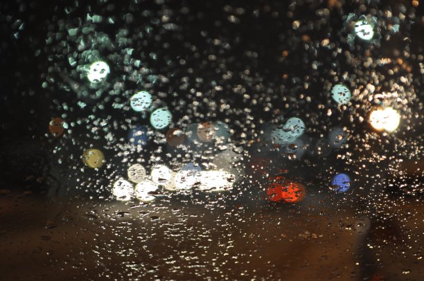 夜晚的城市透过汽车的挡风玻璃。雨滴落在玻璃上图片下载