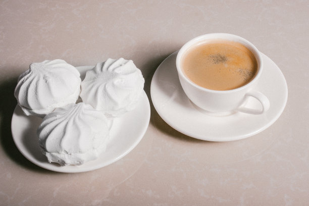 一杯新鲜的咖啡，美式咖啡和三个美味的甜甜点白色棉花糖在碟子上特写。本空间图片下载