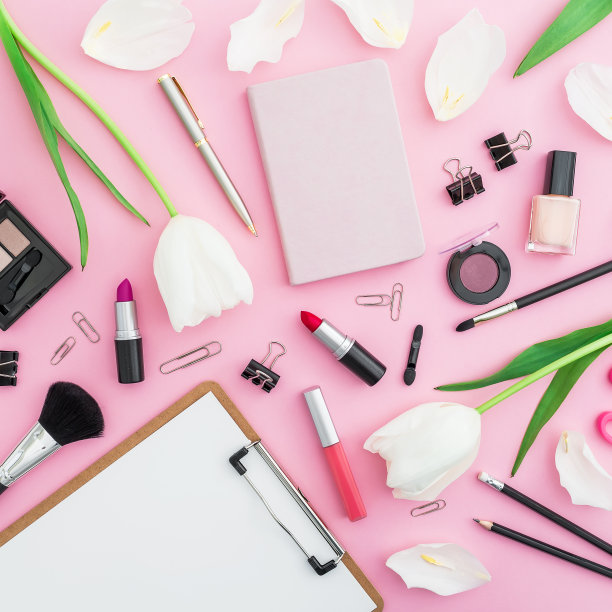 美丽的女博主组成与剪贴板，鲜花，化妆品和配件在粉红色的背景。前视图。平的。图片下载