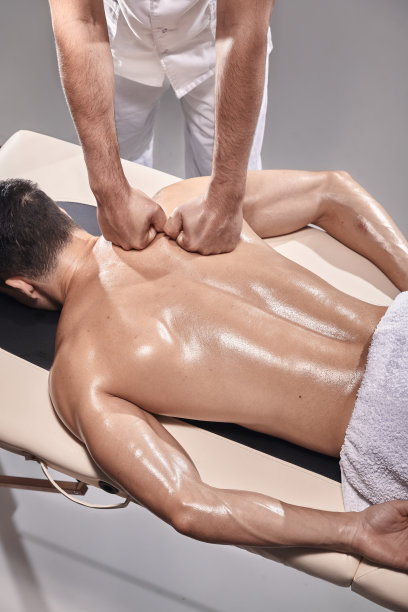 两个年轻人，20-29岁，在室内运动理疗工作室拍摄照片。理疗师用手按摩肌肉发达的病人背部，从高处看。图片下载
