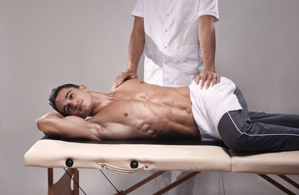 两个年轻人，20-29岁，在室内运动理疗工作室拍摄照片。理疗师用手按摩肌肉病人的背部。图片下载