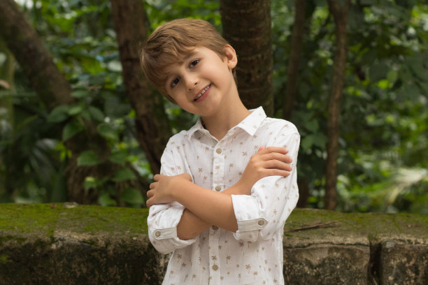 生活方式:一个微笑的小男孩穿着白色的衬衫在绿色的背景。公园里快乐的孩子。金发男孩图片下载