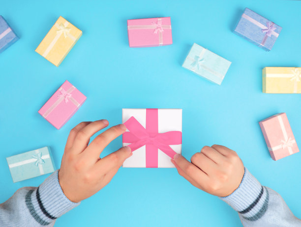 俯视图的手拿着一个小盒子的礼物和一条丝带在一个蓝色的背景。图片下载