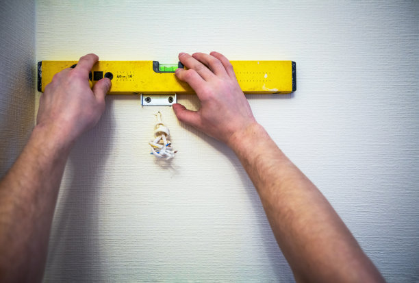 公寓内工人在老黄水位的墙上安装灯或烛台的工作过程正在施工、改造、翻新、修复和重建中。工人手拿着并使用wa测量墙壁准线图片下载