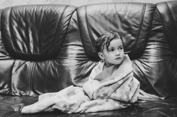 可爱的宝宝盖着毛巾坐在父母的床上，沙发上，沐浴后或淋浴。清洁干燥的孩子在卧室。概念沐浴和清洗的小孩。儿童卫生。黑白照片。图片下载