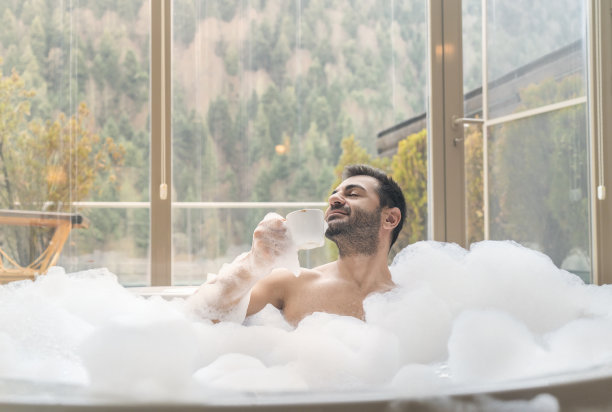 男人在热水浴缸里放松和微笑，喝咖啡/茶图片下载