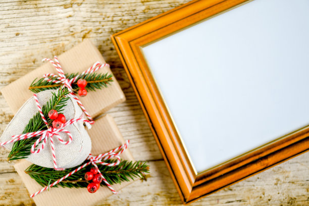 顶视图礼盒手工与棕色纸紧与红和白缎带，绿色的松树叶边与相框的照片图片下载
