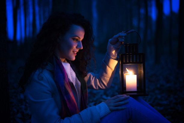 微笑的女人坐在黑暗的树林里提着灯笼图片下载