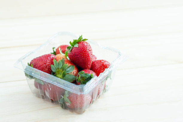 新鲜的红草莓装在木背景的塑料容器里图片下载