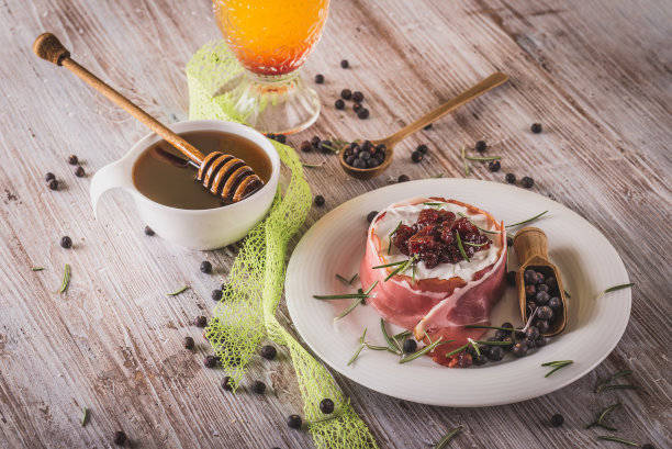 整个卡芒贝尔的水平照片。奶酪包在干火腿里，上面有蔓越莓。白色的盘子上放着奶酪，木板上洒着杜松子果，颜色很旧。图片下载