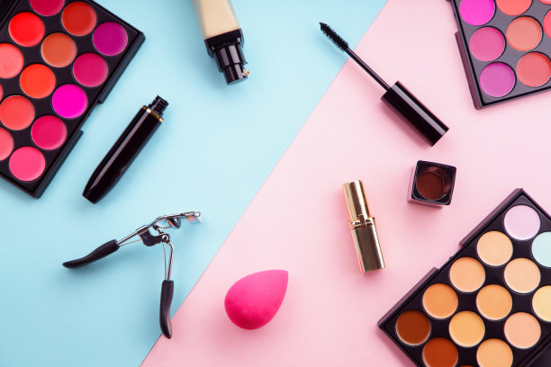 化妆品俯视图图片:口红和遮瑕膏，粉底，睫毛膏和睫毛夹在粉红色和蓝色的背景。化妆师套装概念图片下载