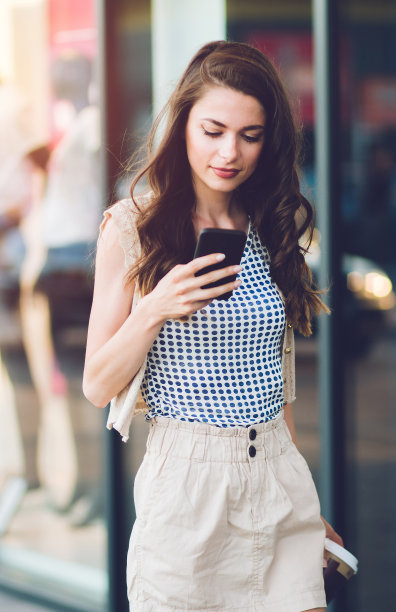 年轻女孩拿着手机在户外城市街道。图片下载
