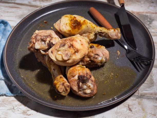 鸡腿放在一个灰色的圆盘子上，在微波炉里煮，牛仔布蓝色的餐巾，餐具。图片下载