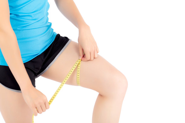 特写白种人腿苗条的女人与测量隔离在白色背景，女孩穿着运动与测量厘米的胶带为健康和饮食，脂肪团和卡路里的保健。图片下载