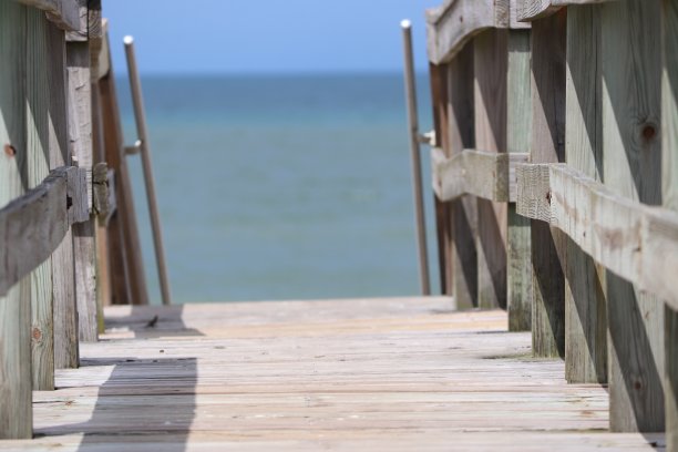 透视照片的木板路栏杆海滩进入地平线，蓝天，蓝绿色的海洋和绿色的草。图片下载
