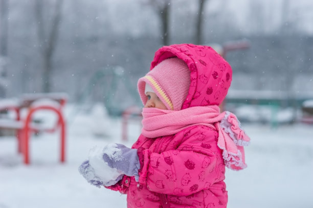 婴儿在冬天的工作服裹着围巾走在白雪覆盖的街道上，用雪雕刻。图片下载