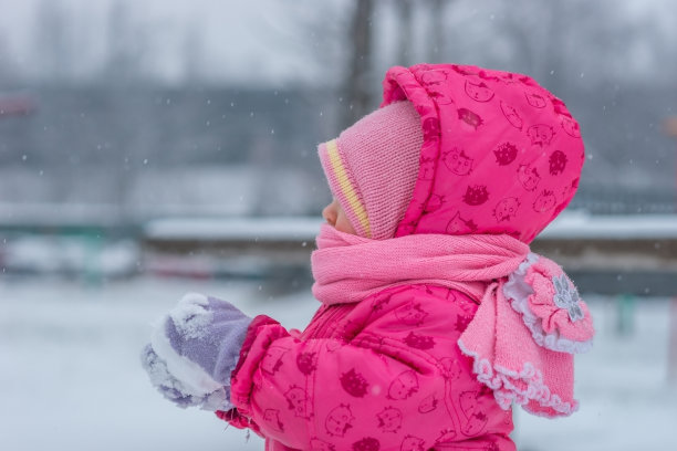 婴儿在冬天的工作服裹着围巾走在白雪覆盖的街道上，用雪雕刻。图片下载
