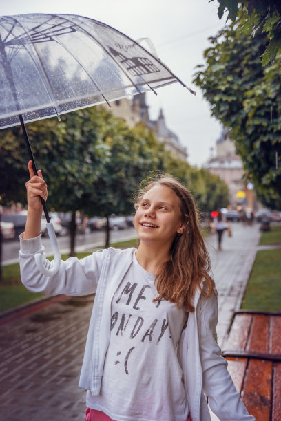 一个女学生撑着伞在雨中行走在城市的小巷里。图片下载