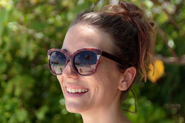 棕榈树，白色的沙滩和晶莹湛蓝的海水倒映在太阳镜上的一个快乐的女人。马尔代夫图片下载