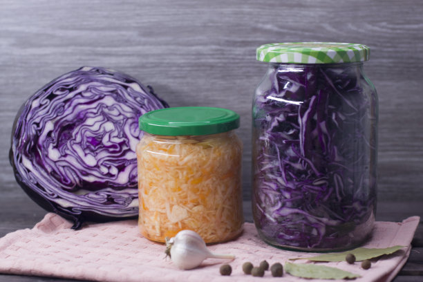 照片中的泡菜和胡萝卜在一个罐子和紫色卷心菜在一个罐子在一个木制的背景。图片下载