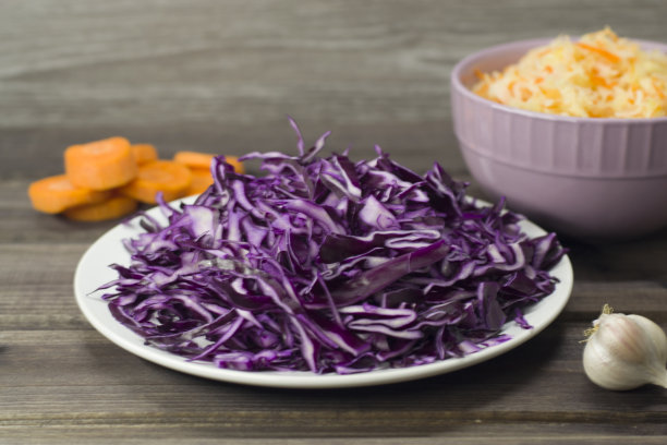 这是一张紫色卷心菜沙拉的特写照片，在深色的木头背景上是盘子里的泡菜和胡萝卜。图片下载