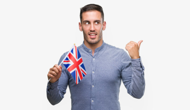英俊的年轻人举着英国国旗，手和手指向上指着，笑脸相迎图片下载