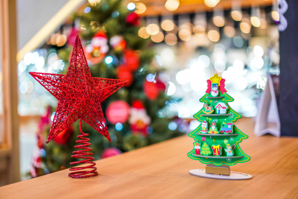 红星和圣诞树纸工艺装饰在木桌上，后面是模糊的大圣诞树。图片下载