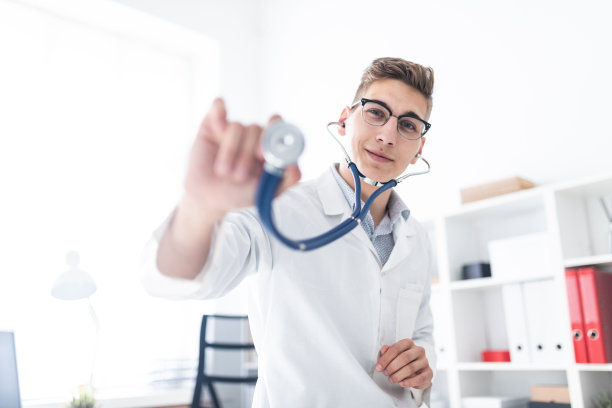 一位身穿白袍的年轻医生靠在办公室的一张桌子上，向前伸着一个声音内窥镜。图片下载