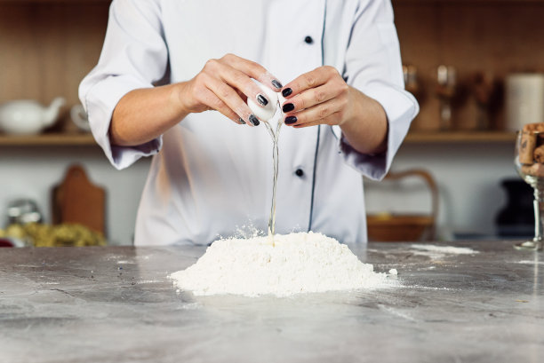 一个女厨师的手，在做面团的时候，将一个鸡蛋打入一堆量好的面粉中。图片下载