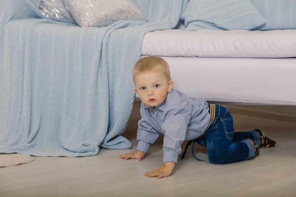 穿着白色针织毛衣，发型时髦的易洛魁人从沙发下爬出来，张着嘴看着镜头。男孩躺在沙发下面的地板上图片下载