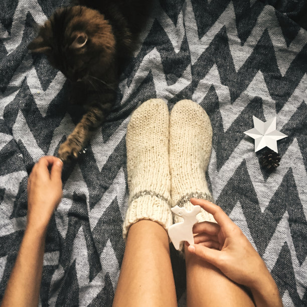 可爱的小猫在女孩的腿上玩圣诞羊毛袜和时髦的驯鹿玩具。前视图。大气舒适的形象，暖冬的心情。手机照片图片下载